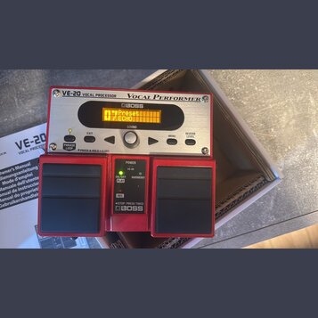 Červený vokální procesor značky BOSS s nápisy VE-20 VOCAL PROCESSOR a Vocal Performer. Zařízení má stříbrný ovládací panel s displejem, na kterém je…