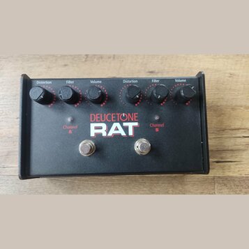 Černý efekt pedál s nápisy DEUCETONE a RAT. Horní panel obsahuje dva identické sady ovládacích prvků s popisky Distortion, Filter a Volume. Ve spodní…