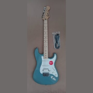 Modrá elektrická kytara typu Stratocaster se světle hnědým hmatníkem a bílým pickguardem. Na hlavě je černý nápis Squier a menší text by Fender. Na t…