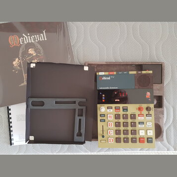 Fotografie zobrazuje elektronický hudební přístroj v hnědém kufru s nápisem Medieval a podtitulem instrumentalia electronicum. Zařízení má béžový pan…