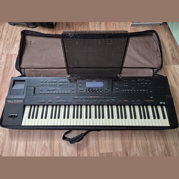 Černý digitální klavír Roland G-800 v černém polstrovaném pouzdře. Na levé straně je nápis Roland G-800 a pod ním text 64 VOICE POLYPHONY. Přístroj o…