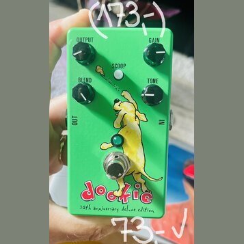 Zelený kytarový efekt s nápisy OUTPUT, GAIN, BLEND a TONE u ovládacích knoflíků. Uprostřed je bílé tlačítko s nápisem SCOOP a obrázek žlutého psa. Ve…
