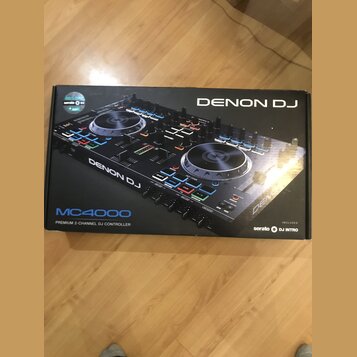 Kartonová krabice s obrázkem černého DJ kontroléru. Na krabici jsou nápisy DENON DJ, MC4000 a PREMIUM 2-CHANNEL DJ CONTROLLER. V pravém dolním rohu j…