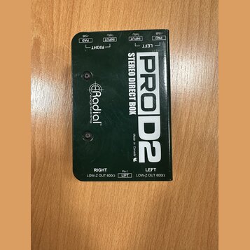 Černá stereo DI box s kovovým povrchem a bílými nápisy. Na horní straně jsou popisky PAD -15dB, INPUT a THRU pro kanály RIGHT a LEFT. Uprostřed je uv…