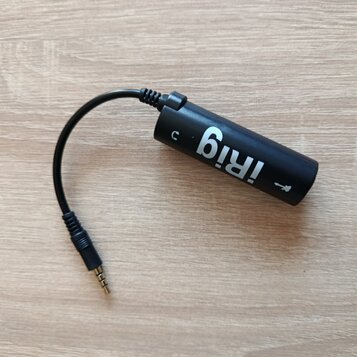 Černý cylindrický audio rozhraní s krátkým integrovaným kabelem zakončeným 3,5mm jack konektorem. Na těle je bílý nápis iRig a symbol v podobě šipky.…