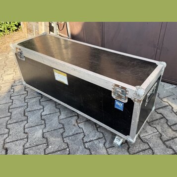 Černý transportní flightcase s hliníkovými hranami a kovovými rohy. Na boku je umístěna žlutá varovná nálepka a modrý štítek s nápisem THON. Povrch v…