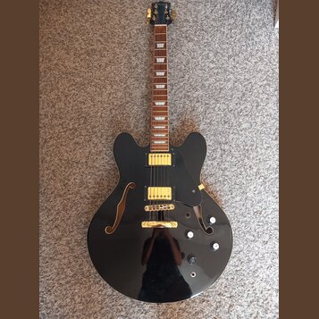 Černá polodupatá elektrická kytara s lesklým povrchem a hnědým hmatníkem. Na hlavě je nápis Epiphone, na krytkách snímačů a mostu jsou zlaté prvky. K…