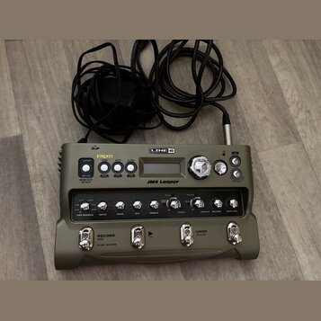 Šedý looper značky LINE 6 s nápisem JM4 Looper. Zařízení má několik ovládacích knoflíků, tlačítka a displej, nad kterým jsou nápisy GUITAR, MIC/AUX,…