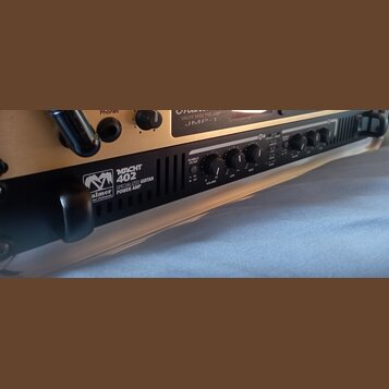 Detailní pohled na přední panel černého zesilovače s nápisy „MACHT 402“ a „SPECIALIZED GUITAR POWER AMP“. Vedle textu je umístěno logo s nápisem „Pal…