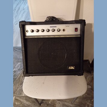 Černý kytarový kombo zesilovač s bílým ovládacím panelem a černou textilní maskou reproduktoru. Na panelu je nápis GUITAR AMPLIFIER, model AK30A a na…