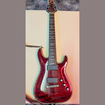 Elektrická kytara s červeným lakovaným tělem s výraznou strukturou dřeva a lemováním. Na hlavě je nápis Schecter. Nástroj má dva humbuckery, tři ovál…
