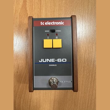 Šedý efekt pedál s dřevěným rámem a červeným horním panelem. Na zařízení jsou nápisy tc electronic, MONO, STEREO, I, II, JUNE-60, CHORUS a TRUE BYPAS…
