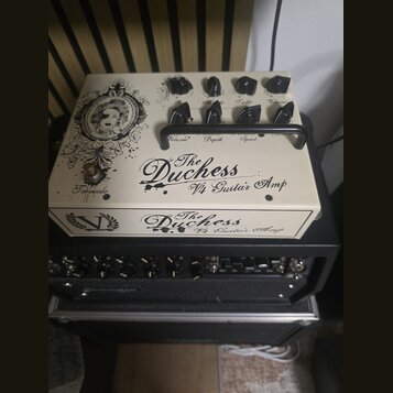 Kremově bílý kytarový zesilovač s černými ovládacími knoflíky a černou rukojetí. Na horní i přední straně je nápis „The Duchess Vt4 Guitar Amp“ a vle…