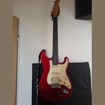 Červená elektrická kytara typu Stratocaster s bílým pickguardem a hnědým hmatníkem. Na hlavě je vidět nápis Squier. Kytara má tři snímače, pětistupňo…