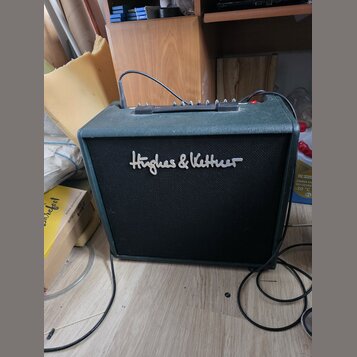 Kytarový kombo zesilovač s tmavě zeleným povrchem z textilu a černou přední síťovkou. Na síťovce je bílý nápis Hughes & Kettner. Horní panel obsahuje…