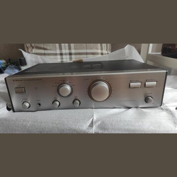Stříbrný integrovaný stereo zesilovač s černým horním krytem a ventilační mřížkou. Na předním panelu jsou nápisy ONKYO, INTEGRATED STEREO AMPLIFIER a…