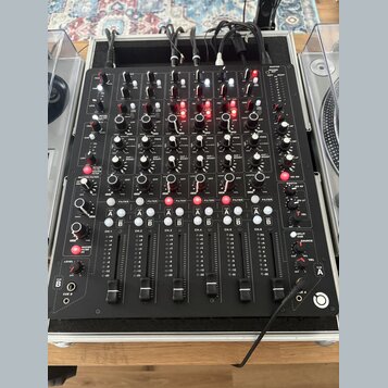 Černý DJ mixér s mnoha ovládacími prvky, potenciometry a posuvníky. Na panelu jsou viditelné nápisy jako MASTER, FILTER, CUT / BOOST, CUE A, CUE B a…