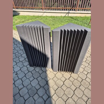 Dvě šedé akustické pěnové panely s žebrovaným povrchem. Panely mají tvar kvádru s vertikálními drážkami a jsou umístěny vedle sebe na dlažbě. Na povr…
