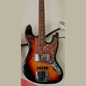 Elektrická basová kytara s korpusem v barevném přechodu od černé přes červenou k žluté. Nástroj má hnědý hmatník a pickguard s červeně-hnědým mramoro…