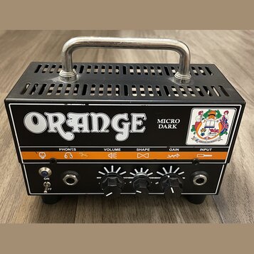Černý kompaktní kytarový zesilovač s kovovou rukojetí nahoře. Na předním panelu je bílý nápis ORANGE a model Micro Dark. Zařízení má čtyři ovládací p…