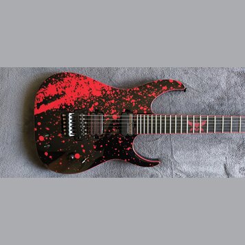 Elektrická kytara s černým povrchem a červenými stříkanci. Na hmatníku je vidět červený znak ve tvaru hvězdy a na kobylce nápis FLOYD ROSE. Kytara má…
