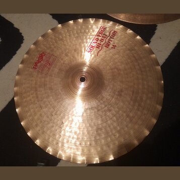 Kovový činel v zlatavé barvě s viditelným klepaným povrchem a vlnitým okrajem. Na povrchu je červený nápis SOUND EDGE HI-HAT BOTTOM 14" a logo Paiste…