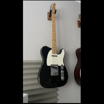 Černá elektrická kytara typu Telecaster s bílým pickguardem a světlou hmatníkovou deskou. Nástroj vykazuje známky opotřebení v podobě odlakování na s…