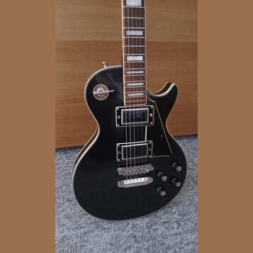 Černá elektrická kytara typu Les Paul s bílým lemováním. Na krytce horního snímače je nápis "Les Paul". Kytara má dva humbuckery, čtyři ovládací knof…
