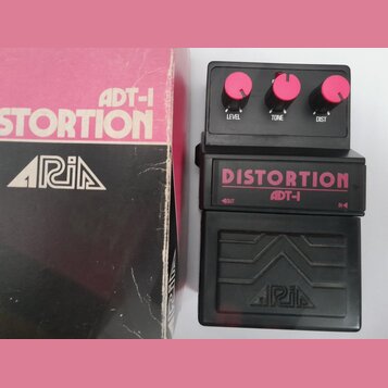 Černý kytarový efekt s nápisem DISTORTION ADT-1 a třemi růžovými oválnými knoflíky s popisky LEVEL, TONE a DIST. Pod efektem je černý plastový kryt s…