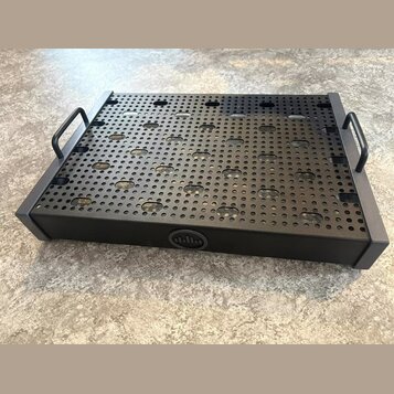 Černý kovový pedalboard s perforovaným vrchem a dvěma bočními madly. Na přední hraně je umístěn kulatý emblem s logem znázorňujícím stylizované sloup…