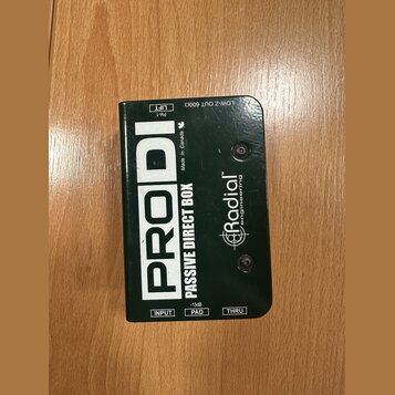Černá pasivní DI box s nápisy PRODI a PASSIVE DIRECT BOX. Na povrchu je logo Radial engineering a text Made in Canada. Jsou zde viditelné popisky vst…