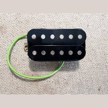 Černý humbucker s dvěma řadami šesti stříbrných pólů. K snímači vede zelený izolovaný kabel. Povrch je hladký a černý, bez viditelných značek, log ne…