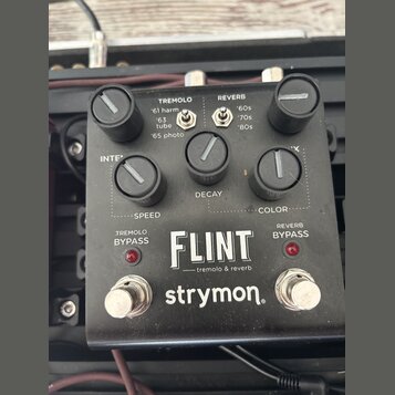 Černý kytarový efekt pedál s nápisy FLINT, tremolo & reverb a značkou strymon. Na horní části jsou tři černé ovládací knoflíky s popisky SPEED, DECAY…