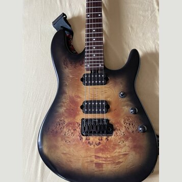 Elektrická kytara s tělem z masivu s viditnou strukturou dřeva a černým přechodem k okrajům (burst). Nástroj má dva černé humbuckery, hmatník s bílým…