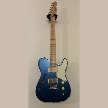 Modře lakovaná elektrická kytara s dutým korpusem a f-otvorem. Na hlavě hmatníku je nápis Squier a modelové označení Telecaster. Nástroj má světlý dř…