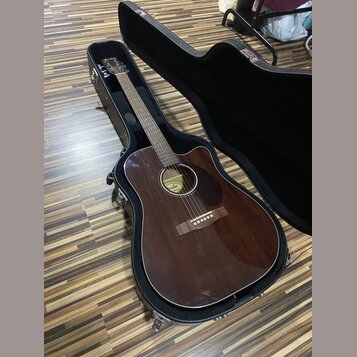 Tmavně hnědá akustická kytara v černém tvrdém kufru. Na hmatníku je vidět nápis Fender Acoustic. Povrch nástroje je glossy, bez viditelných poškzení.