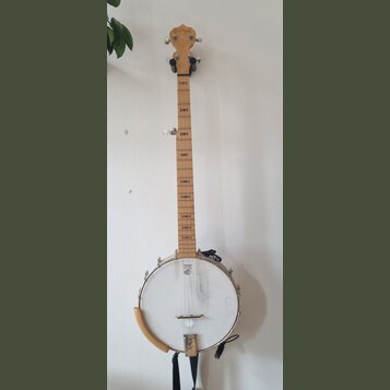Světle hnědý banjo s bílou membránou a kovovým obručem. Na hlavě hmatníku je nápis GOODTIME. Membrána vykazuje známky opotřebení v podobě šmouh a v p…