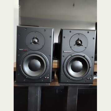 Dva černé studiové monitory v hranatých skříních. Na obou je umístěn nápis dynaudio acoustics. Každý reproduktor má v horní části výšek s kovovou mří…