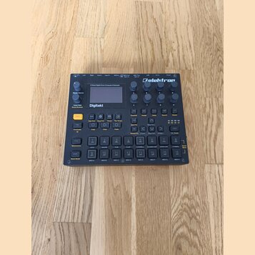 Šedý digitální sampler a sekvencer značky Elektron, model Digitakt. Zařízení má černé ovládací prvky, včetně 16 podsvícených padů a několika otočných…