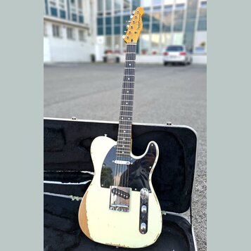Elektrická kytara typu Telecaster v krémové barvě s černým pickguardem, umístěná v otevřeném černém tvrdém kufru. Na hlavě hmatníku je viditelné logo…