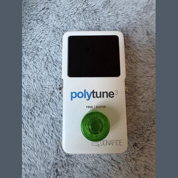 Bílý efekt pedál s černým displejem a zeleným plastovým ovratovcem. Na přední straně je modrý nápis polytune3 a pod ním text TRUE BUFFER. V dolní čás…