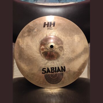 Kovový činel typu splash v zlatavé barvě s viditelným broušením. Na povrchu jsou nápisy HH, Splash 12"/30cm a logo SABIAN s doprovodnými oblouky. Pov…