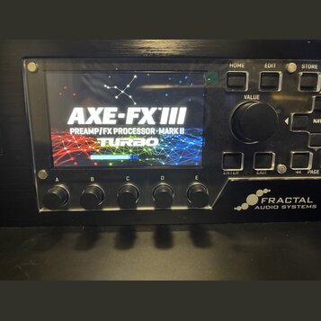 Černý rackový procesor s displejem, na kterém je nápis AXE-FX III PREAMP/FX PROCESSOR MARK II TURBO. V pravém dolním rohu je bílé logo a nápis FRACTA…