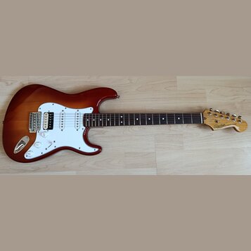 Elektrická kytara typu Stratocaster s tělem v červeně-žlutém sunburst odstínu a bílým pickguardem. Na hlavě hmatníku je vidět nápis Squier STRATOCAST…