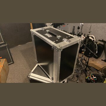 Černý transportní flightcase s hliníkovými hranami a kovovými rohy. Na horní straně je umístěna černá rukojeť a dva kovové zámky, vedle nich je nálep…