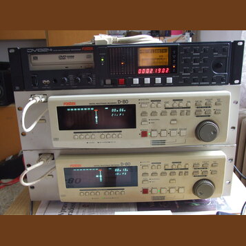 Tři stohované rackové jednotky značky Fostex. Horní zařízení je černý DVD MULTITRACK RECORDER s označením DV824, který má v displeji nápis No files!-…