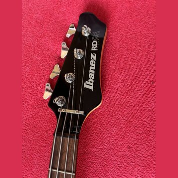 Detail hlavy černé basové kytary s nápisem Ibanez RDGR ROADSTAR. Na hlavě jsou čtyři chromované ladičky a viditelný nápis Ibanez RDGR ROADSTAR v bílé…