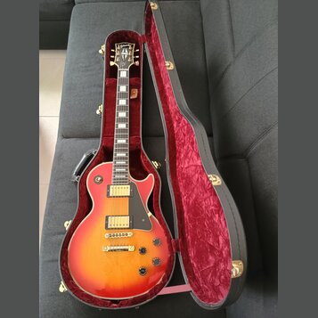 Elektrická kytara typu Les Paul s červeno-žlutým sunburst povrchem v černém tvrdém kufru s červeným plyšovým vnitřkem. Na hlavě hmatníku je nápis Gib…