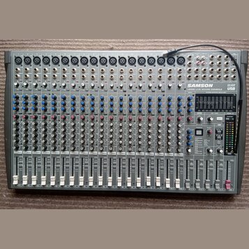 Šedý mixovací pult s nápisy SAMSON, L2000 LIVE MIXING CONSOLE a 24 DSP USB. Zařízení obsahuje řadu vstupních kanálů s modrými a červenými knoflíky, p…