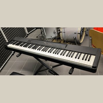 Černý digitální klavír umístěný na černém X-stojanu. Na horním ovládacím panelu je vidět bílý nápis YAMAHA a modelové označení PSR-S970. Nástroj má s…